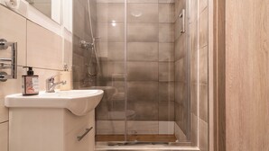 Ein modernes Badezimmer mit Duschkabine aus Glas, einem weißen Waschbecken und einem Holzausziehtisch.
