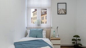 Een slaapkamer met een bed, nachtkastje, raam en een potplant.