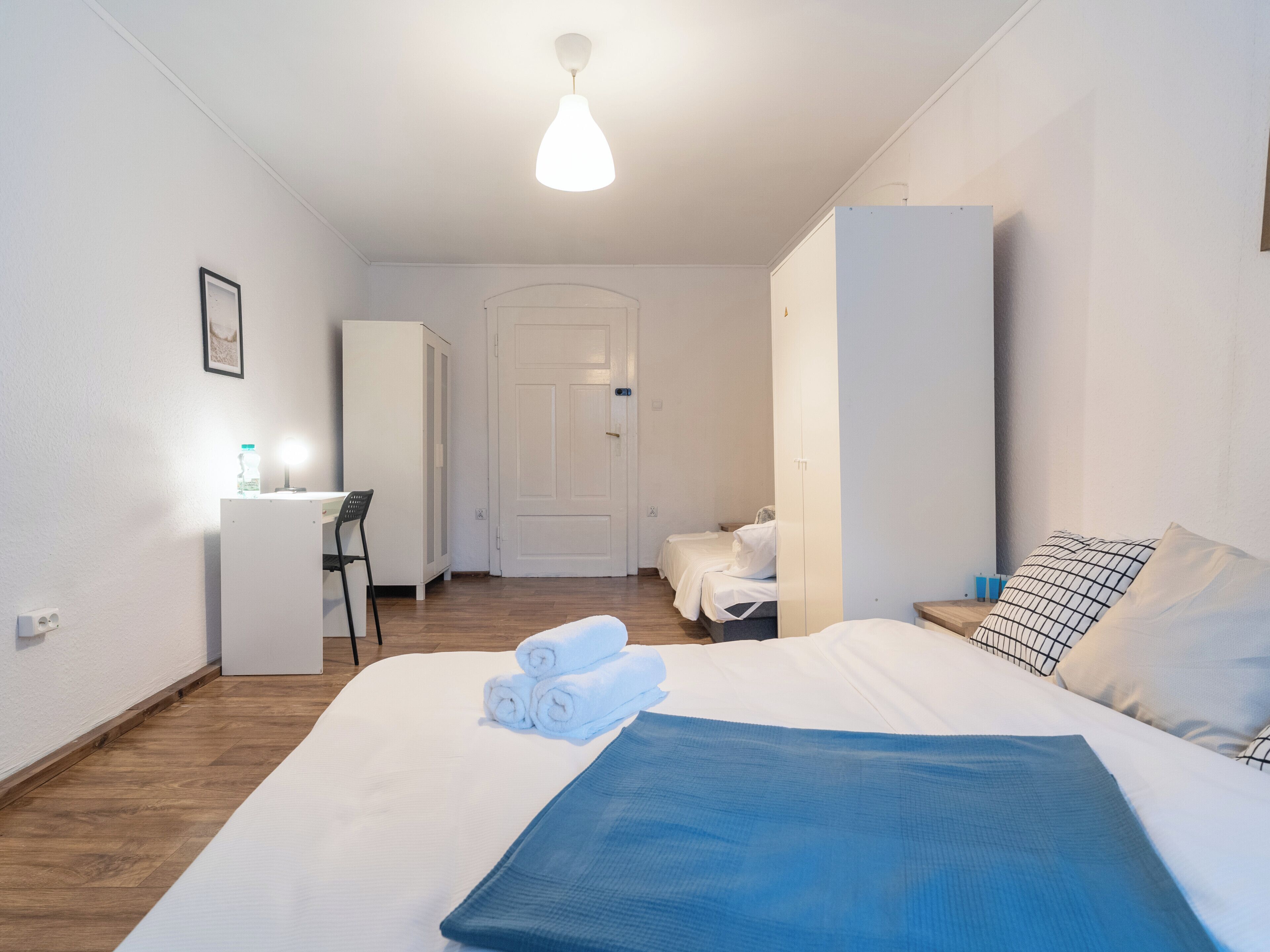A hotel room with a bed, a desk, a chair, and a wardrobe.