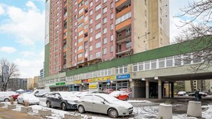 A multi-story building with a green storefront, including a Pepsi sign, and several parked cars in front. - Solidarności City View Apartment (Warszawa)