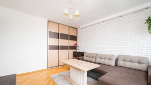 A modern living room with a wooden floor, a sofa, a table, and a white brick wall. - Solidarności City View Apartment (Warszawa)