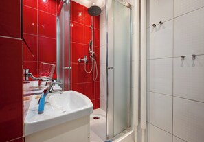 Une salle de bain avec une douche à parois de verre, un lavabo blanc et des murs recouverts de carreaux rouges.