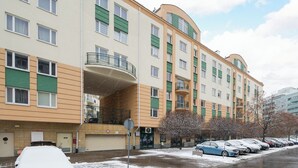 Un immeuble résidentiel à plusieurs étages, doté de balcons, d’un espace de stationnement et d’un sol recouvert de neige.