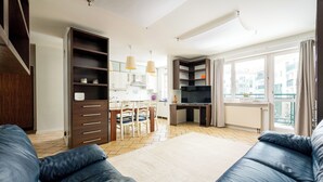 Un salon moderne comprenant un ensemble de canapés, un coin repas avec des chaises et une table, et un espace cuisine avec des placards et un téléviseur.