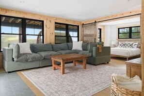 Un salon moderne avec un canapé d’angle, une table basse en bois et un lit doté d’une tête de lit à motifs.