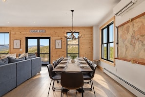 Un coin repas avec une longue table dressée pour six personnes, un canapé et une vue sur l’extérieur.