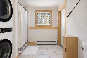 Une buanderie équipée d’un lave-linge, d’un sèche-linge et d’une fenêtre avec des stores.