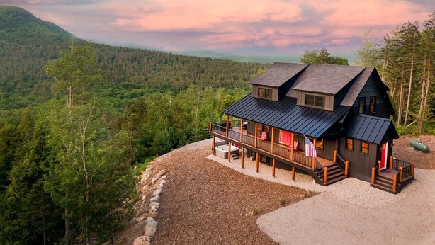 Une cabane dotée d’une terrasse, entourée de forêt, et offrant une vue sur les montagnes.