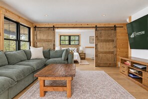 Ein modernes Wohnzimmer mit einem Ecksofa, einem Holztisch und einem großen Fernsehbildschirm.