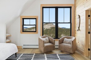 Une chambre avec une grande fenêtre, un lit, deux fauteuils, un tapis et des murs en bois.