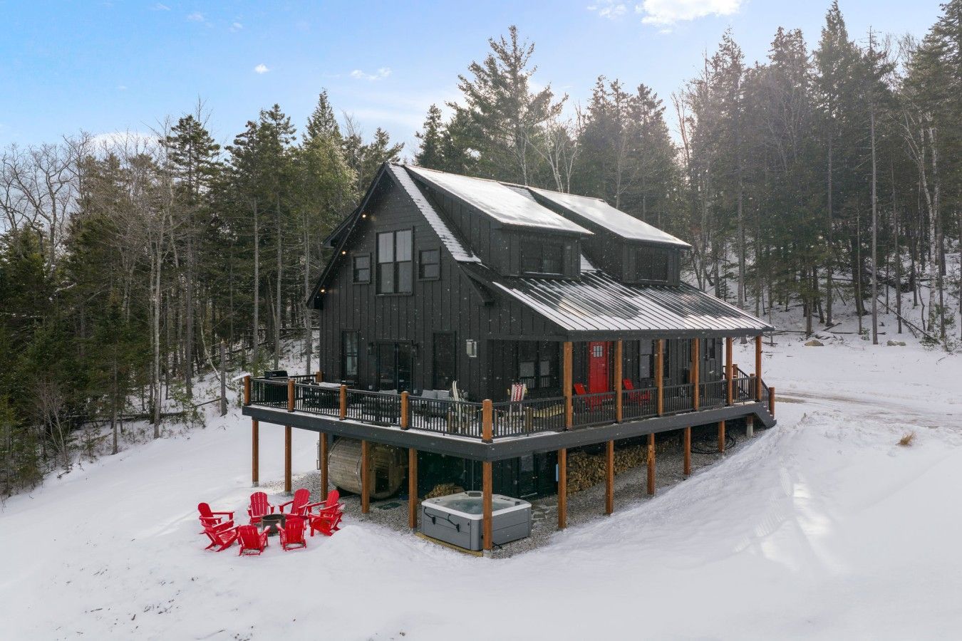 A cabin with a deck and outdoor seating, surrounded by a snowy landscape and trees.