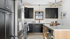 Une cuisine moderne avec des meubles de couleur sombre, des appareils électroménagers en acier inoxydable et un îlot central en bois.