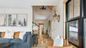 Un salon moderne avec un canapé gris, un fauteuil en cuir marron et une grande fenêtre donnant sur un paysage enneigé.
