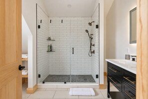 Une salle de bain moderne avec une douche à parois de verre, des carreaux de métro blancs et un meuble-lavabo noir doté de poignées dorées.