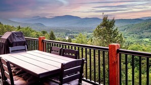 Une terrasse en bois avec une table et des chaises, offrant une vue sur un paysage montagneux.