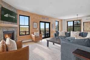 Ein geräumiges Wohnzimmer mit Kamin, einer großen Sofagarnitur und einer Holzwand mit dem Schriftzug 'SUNDAY RIVER'.