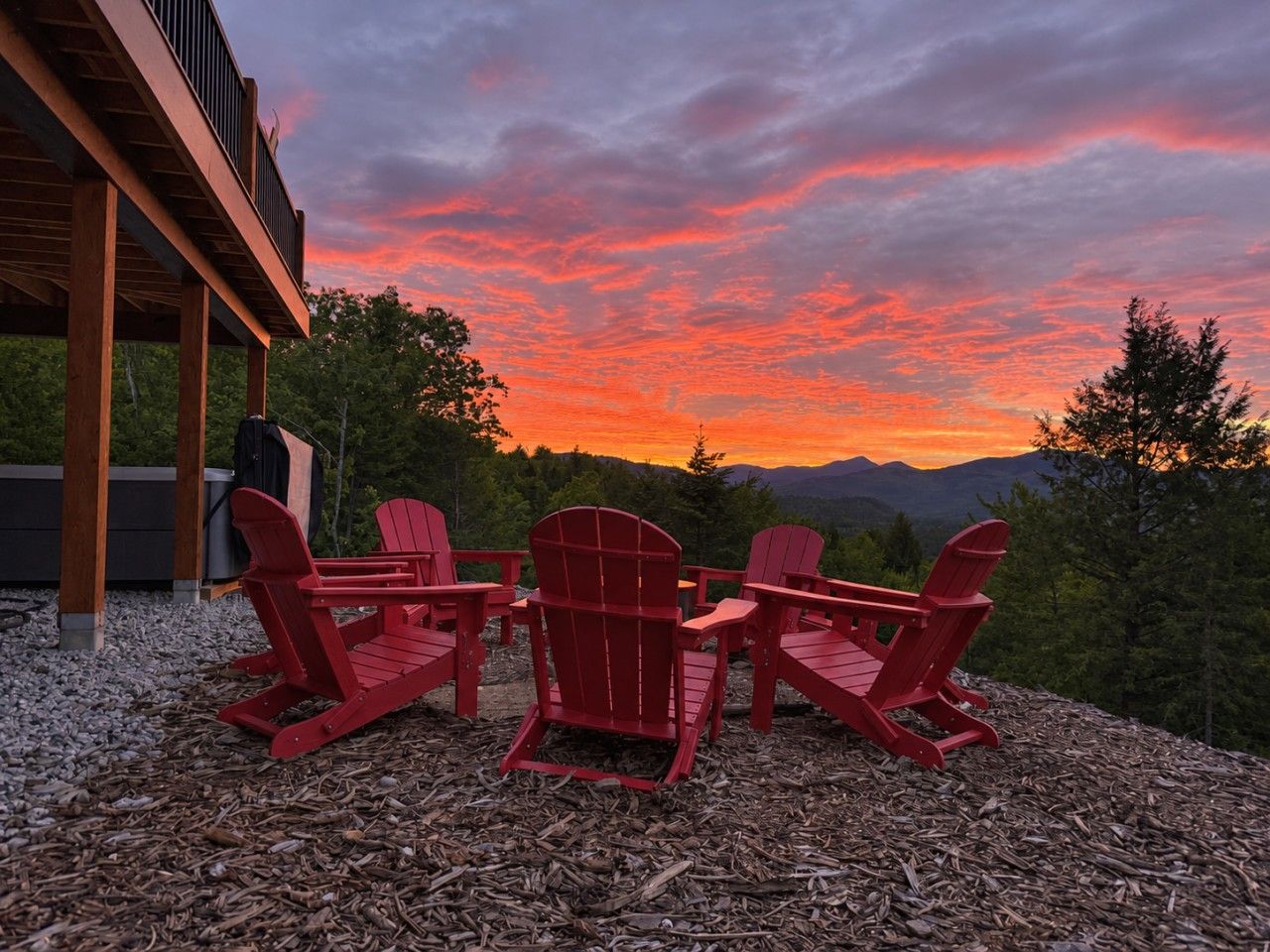 A deck with Adirondack chairs overlooking a mountainous landscape during sunset.