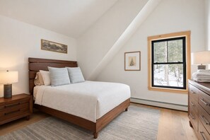 A bedroom with a bed, nightstand, dresser, and a window with a view of trees.