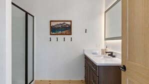 Een moderne badkamer met een douchecabine van glas, een houten kastje met een wastafel en een lijstwerk schilderij van een landschap aan de muur.