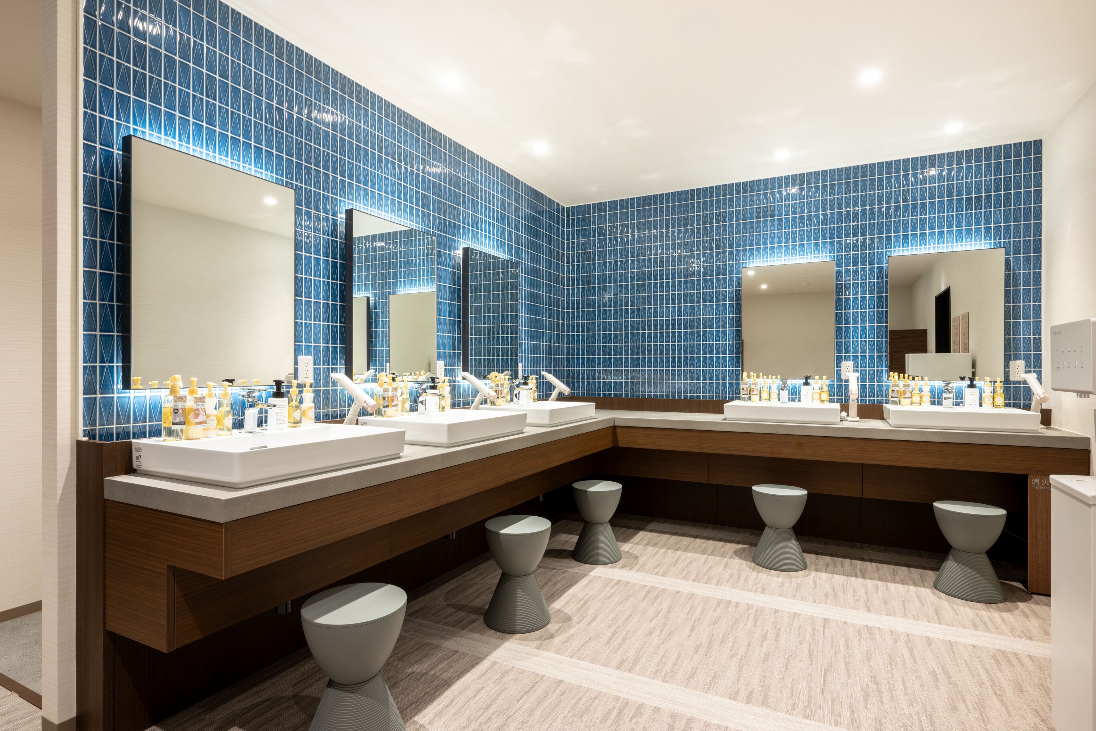 Un baño moderno con paredes de azulejos azules, varios lavamanos y un espejo grande.