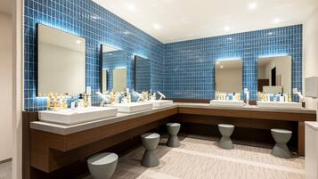 Un baño moderno con paredes de azulejos azules, varios lavamanos y un espejo grande.