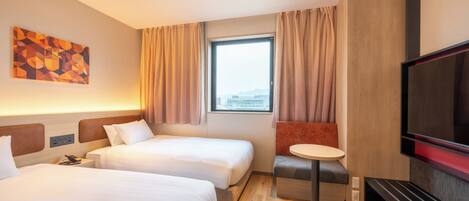Habitación de hotel con dos camas, televisión, una mesita y ventana con cortinas.