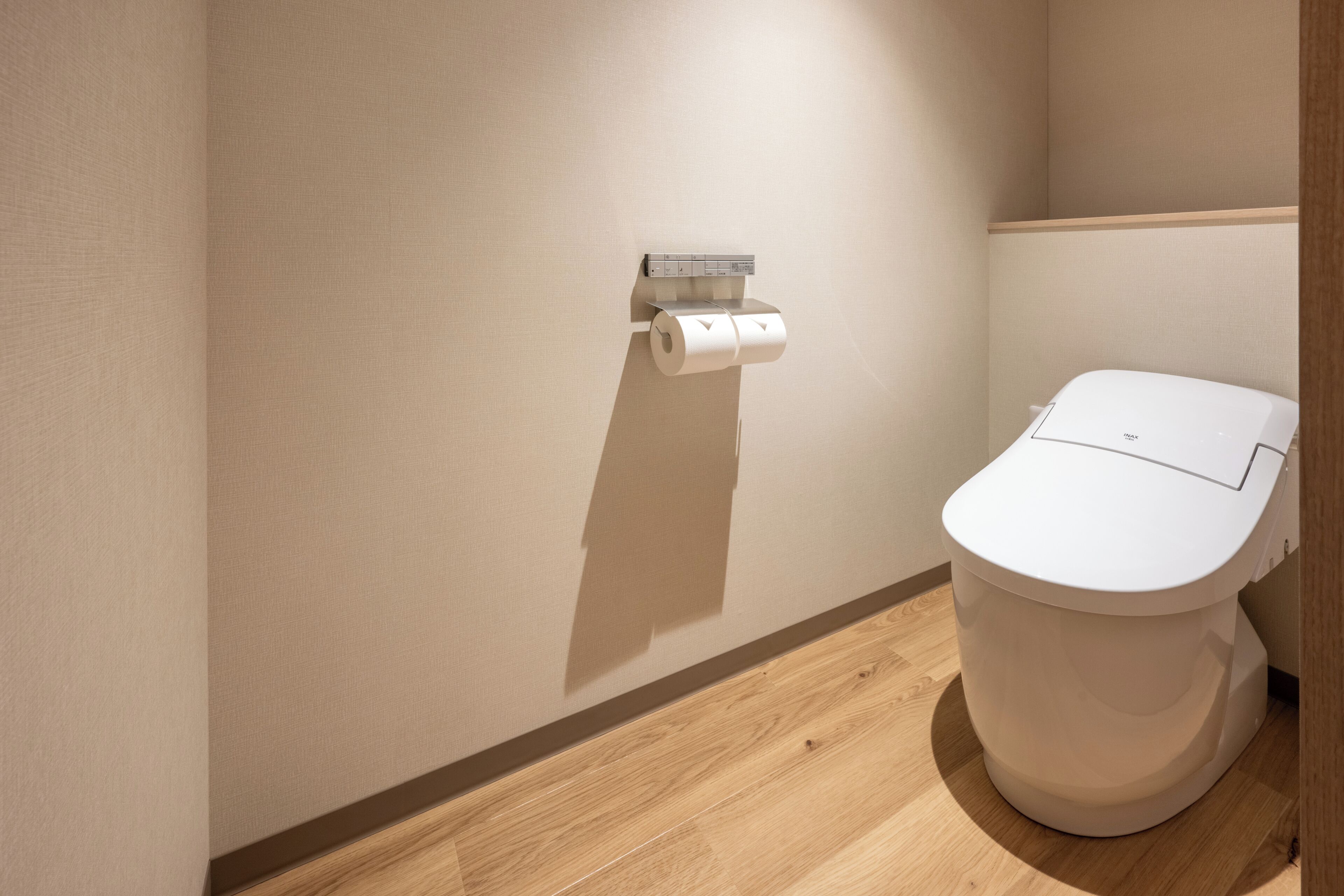 Ein modernes Badezimmer mit Toilette, Toilettenpapierhalter und Holzboden.