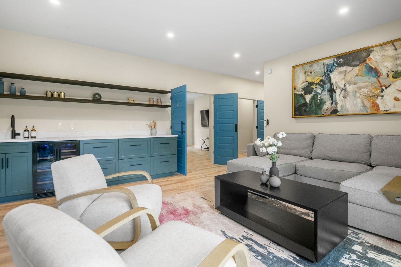 A modern living room with a grey sofa, white armchairs, a black coffee table, and a painting on the wall.