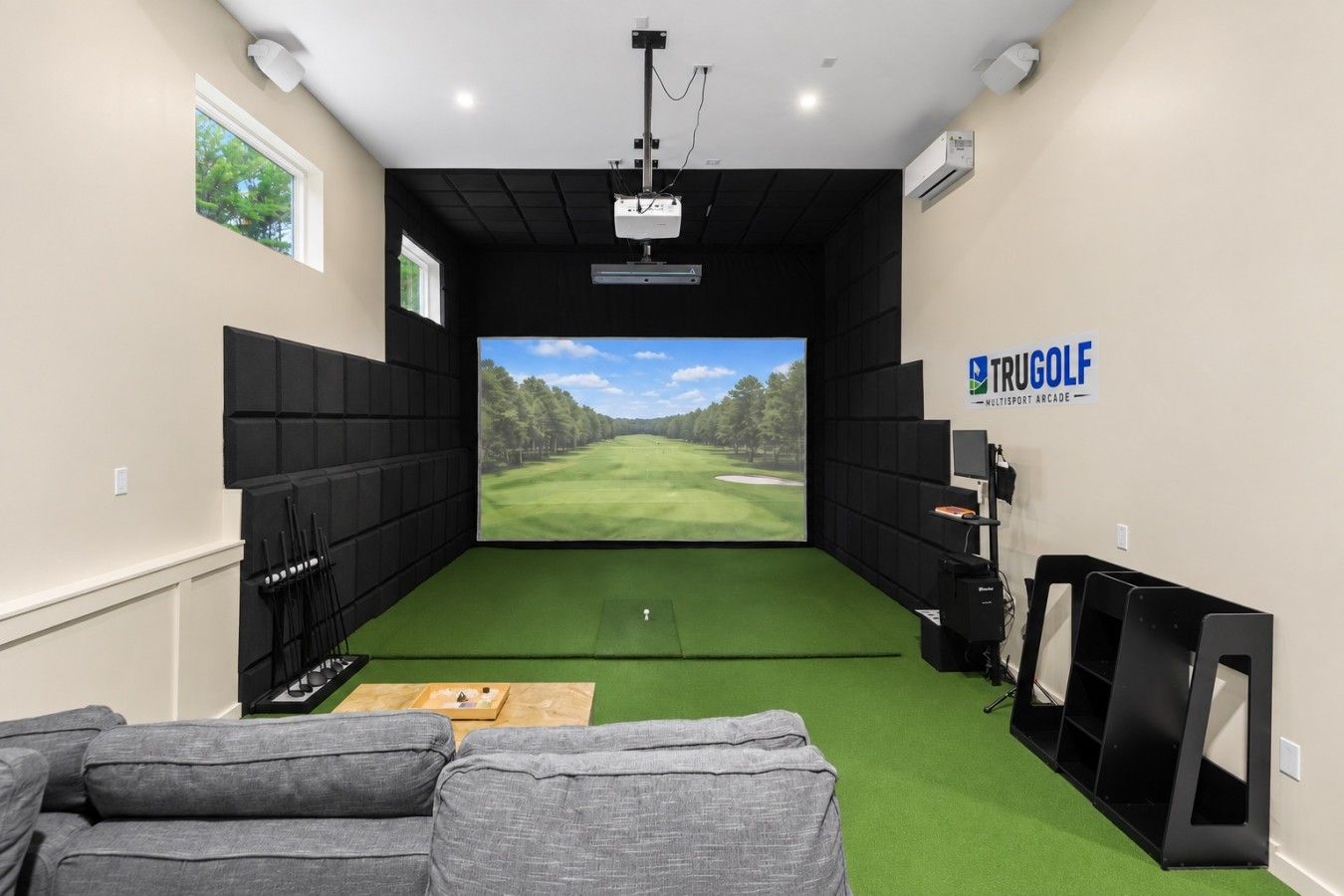 Une pièce dotée d’un grand écran affichant un parcours de golf, un chariot de golf et un projecteur fixé au plafond.