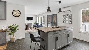 Een moderne keuken met een centraal eiland, barkrukken, een eethoek met een televisie en een groot raam.
