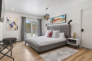 A modern bedroom with a large bed, a side table, a chair, a balcony, and artwork on the walls. - Epic House for Groups: 10 Mins to Sunday River (Bethel)