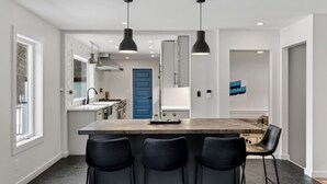 Een moderne keuken met een centraal eiland, zwarte barkrukken, hanglampen en een blauwe deur.