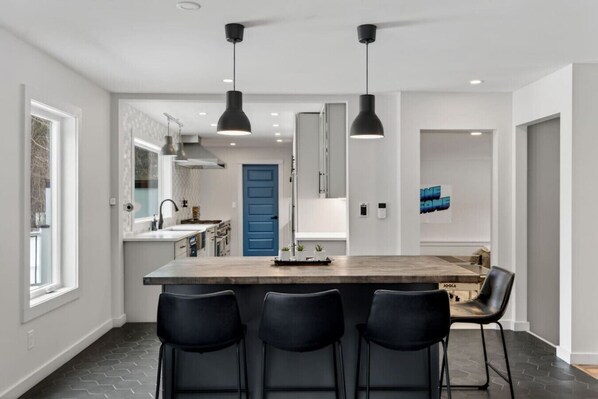 A modern kitchen with a central island, black bar stools, pendant lighting, and a blue door. - Epic House for Groups: 10 Mins to Sunday River (Bethel)