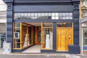 Der Eingang eines Boutique-Hotels mit dunkler Fassade, großen Glasfenstern und einer Holztür.