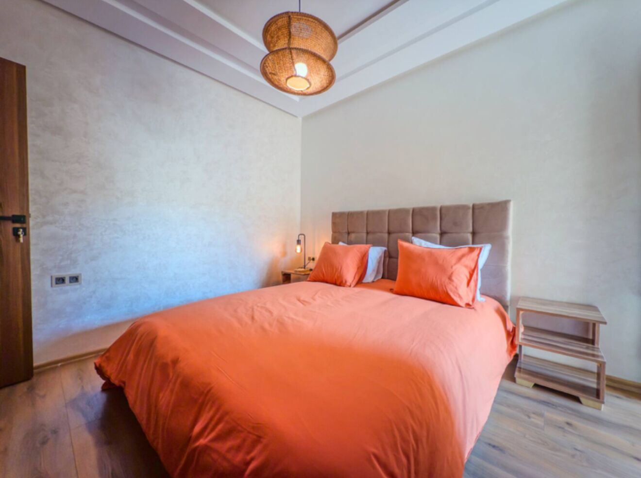 A bedroom with a large bed, a headboard, a bedside table, and a hanging light fixture.