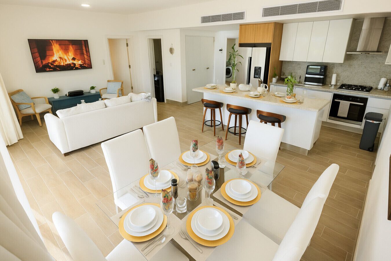 Uma cozinha moderna com armários brancos, uma ilha central e um espaço de refeições com louça branca e dourada.