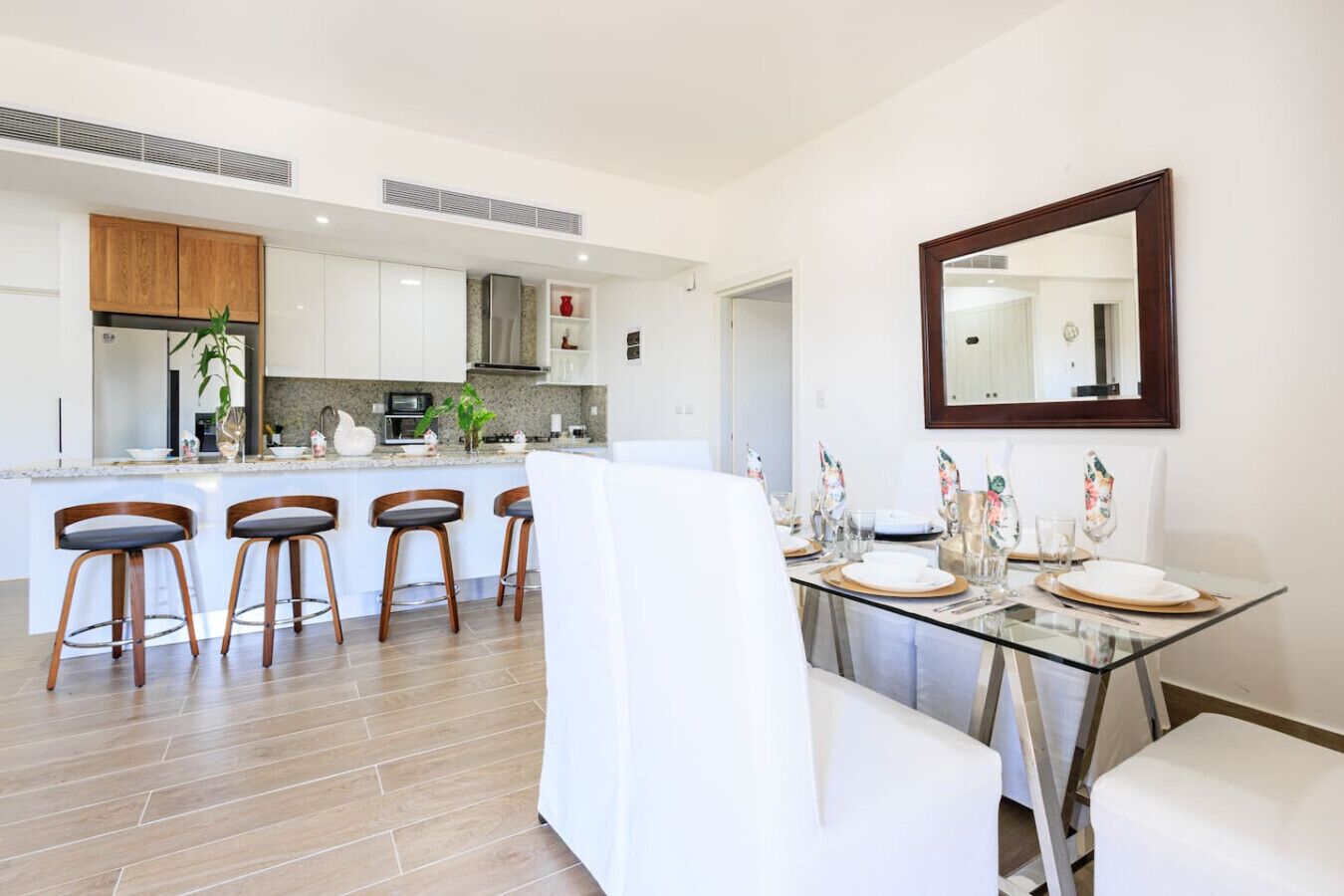 Une cuisine moderne avec des meubles blancs, un îlot central doté de tabourets de bar et un coin repas avec une table et des chaises en verre.