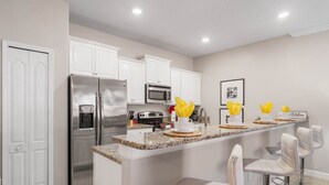A modern kitchen with white cabinets, stainless steel appliances, and a central island with bar stools. - Paradise 4Bd w Private Pool & Waterpark 2941 (Kissimmee)