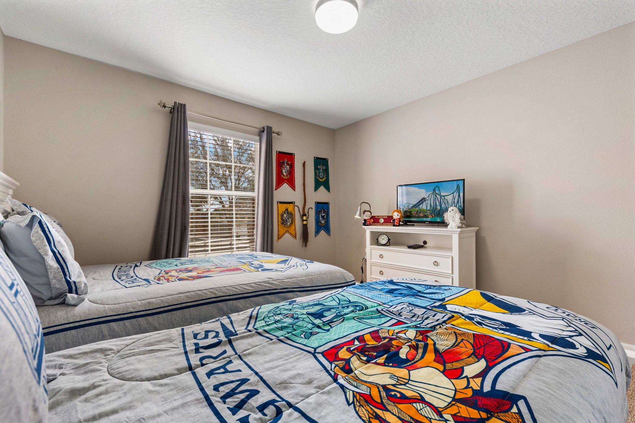 A bedroom with two beds, a window with curtains, a dresser, and wall decorations.