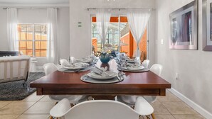 A dining area with a wooden table set for six, white chairs, and a vase of flowers. - Paradise 4Bd w Private Pool & Waterpark 2941 (Kissimmee)