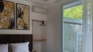 A bedroom with a bed, a wooden headboard, a wall-mounted air conditioner, and a view of a bathroom through a glass door. - Udãra Hideaway Villa (Penida Island)