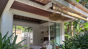 A modern bedroom with a large bed, a sitting area with a table and chairs, and a view of the outdoors. - Udãra Hideaway Villa (Penida Island)