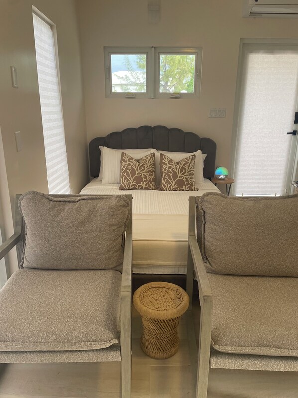 Quarto com uma cama, duas cadeiras, uma mesa redonda pequena e duas janelas.