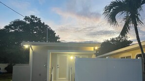 A small, enclosed structure with a door and steps leading to an entrance, surrounded by a white fence and palm trees. - Modern studio in Grand Cayman, West Bay w / private patio & short walk to beach! (West Bay)