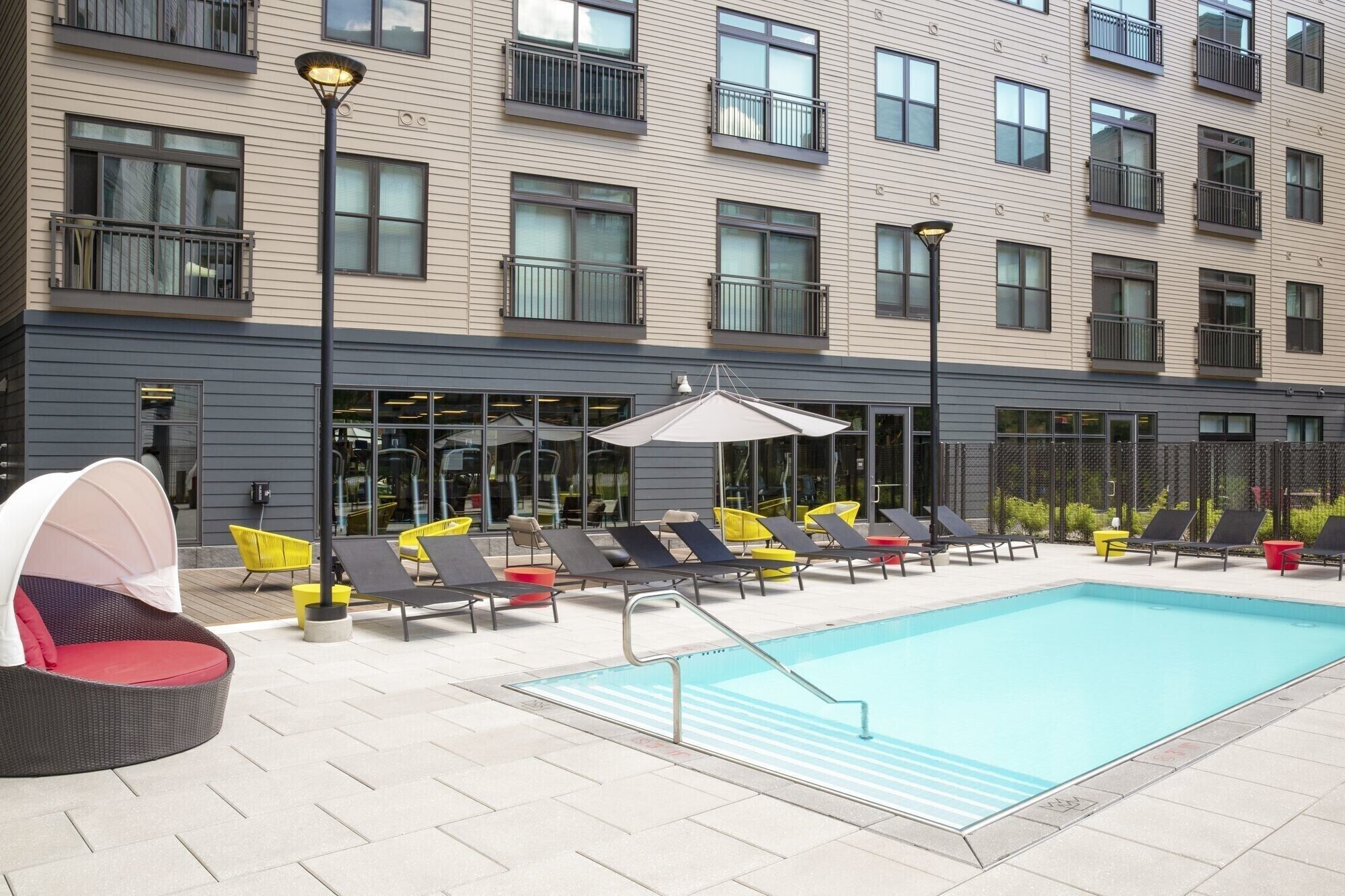 Un hotel moderno con piscina, mobiliario exterior y un área techada.