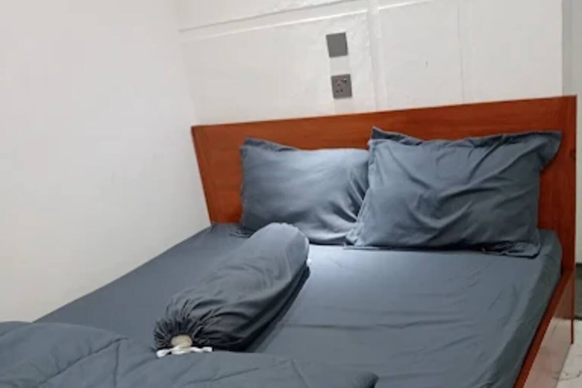 A single bed with a wooden headboard, grey bedding, and a small decorative item on the bed.