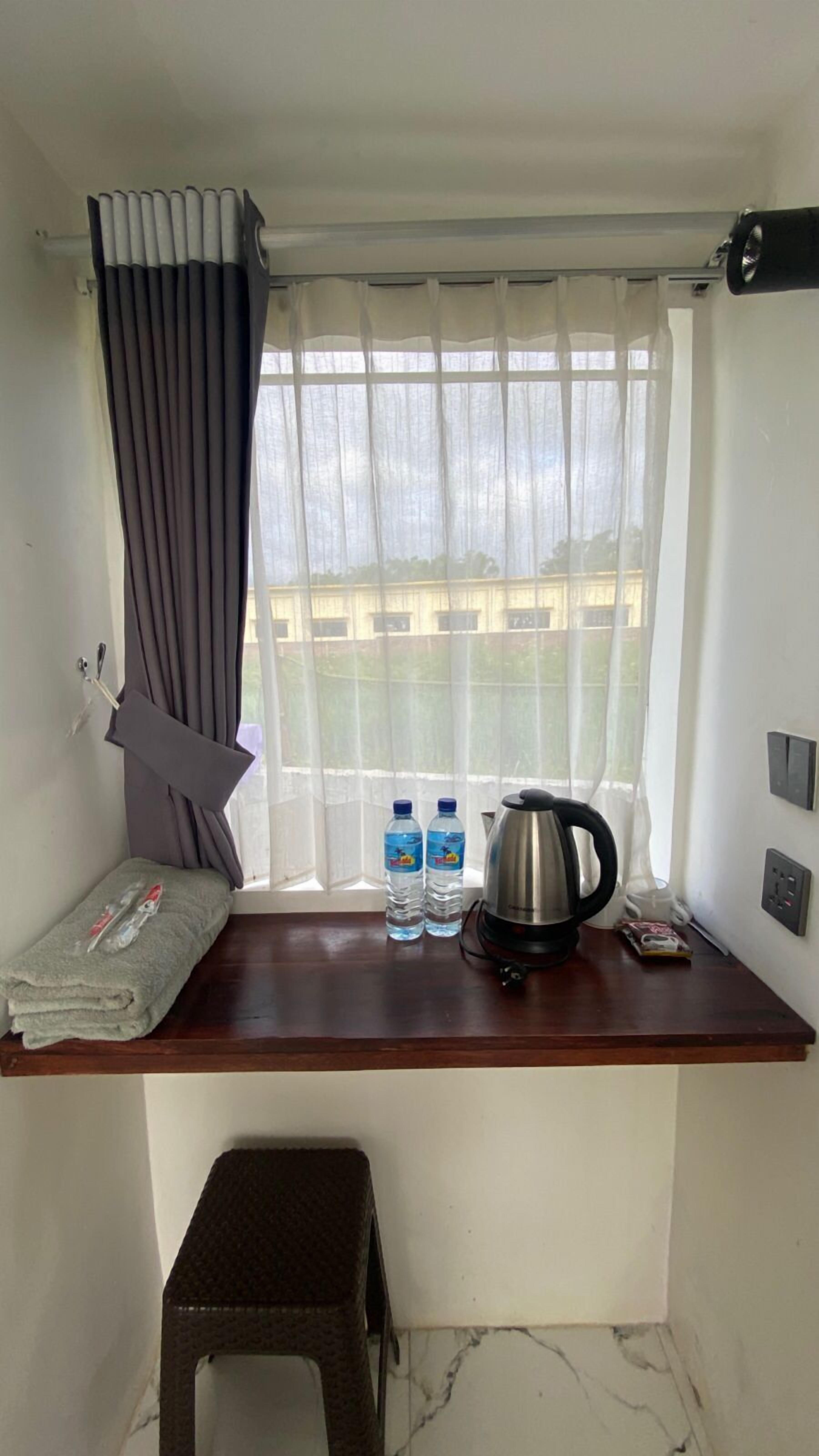 A small room with a window, a wooden table, a kettle, two water bottles, and a folded towel.