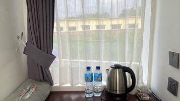 A small room with a window, a wooden table, a kettle, two water bottles, and a folded towel.