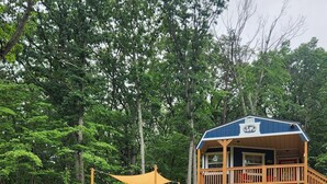 A wooden cabin with a deck, surrounded by a grassy area and trees.