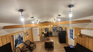 A spacious room with wooden walls and ceiling, a dining area with a table and chairs, and a kitchen area with modern appliances.